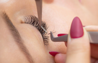 Meister der Wimpernverlängerung setzt falsche Wimpern auf das Augenlid der Frau